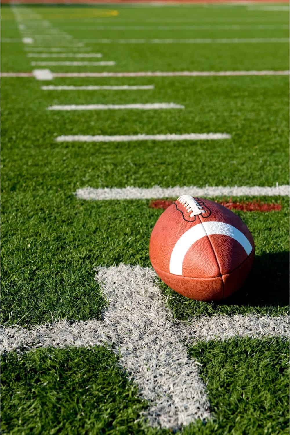 A football rests on the green Vegas Artificial Turf, marked with white yard lines. The laces of the football are visible, and the sunlight casts a shadow on the grass, highlighting the texture of this lush surface.